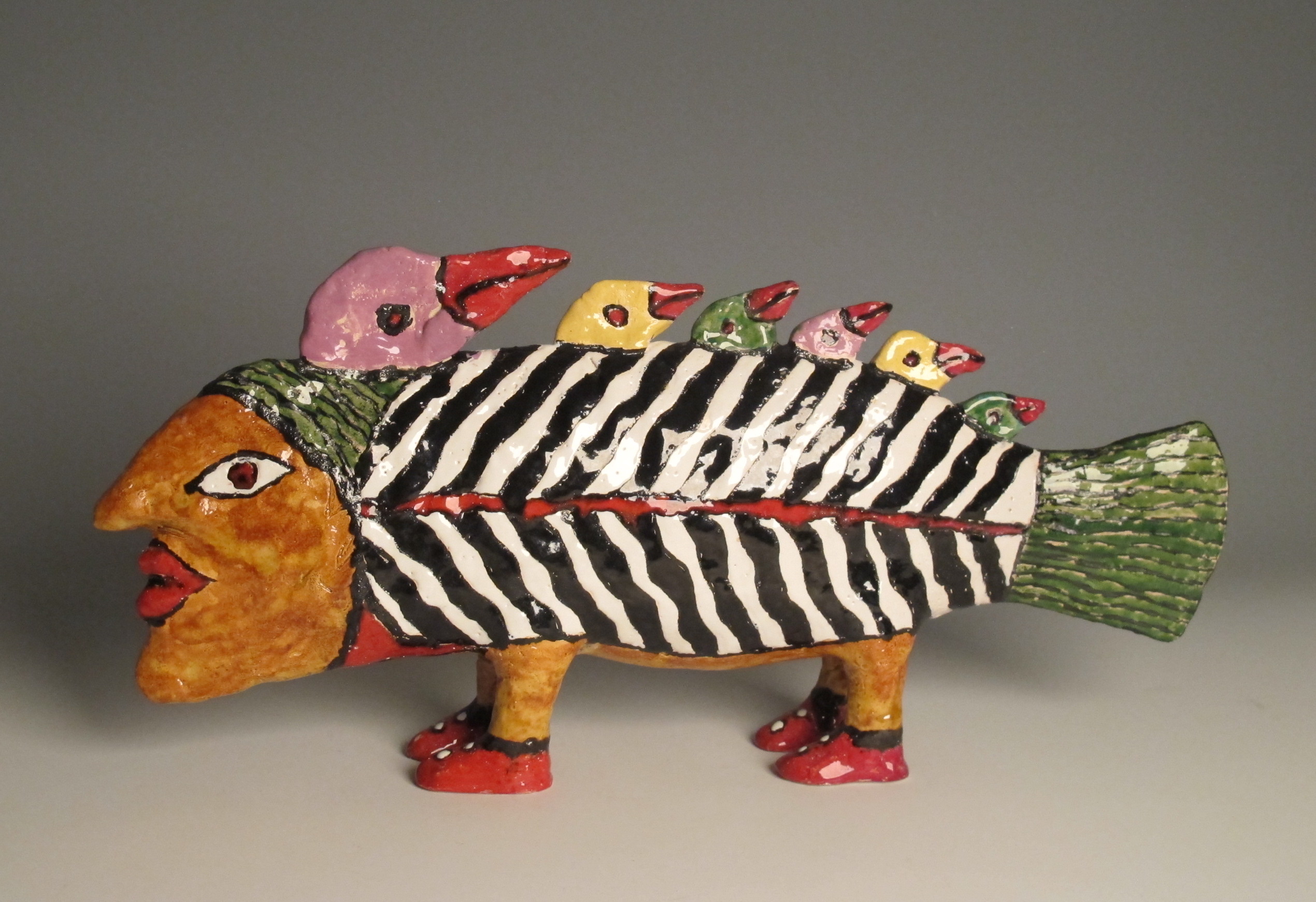 Nelli Isupov, "Fish" - a ceramic fish sculpture with a human face, feet in red shoes, and seven bird heads sticking out the top